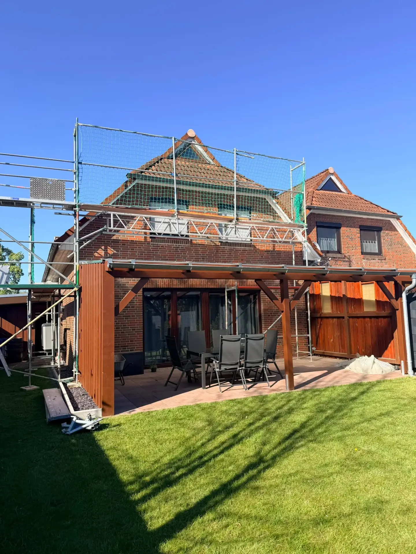 Eingerüstete Rückseite eines Einfamilienhauses mit Klinkerfassade und Garten