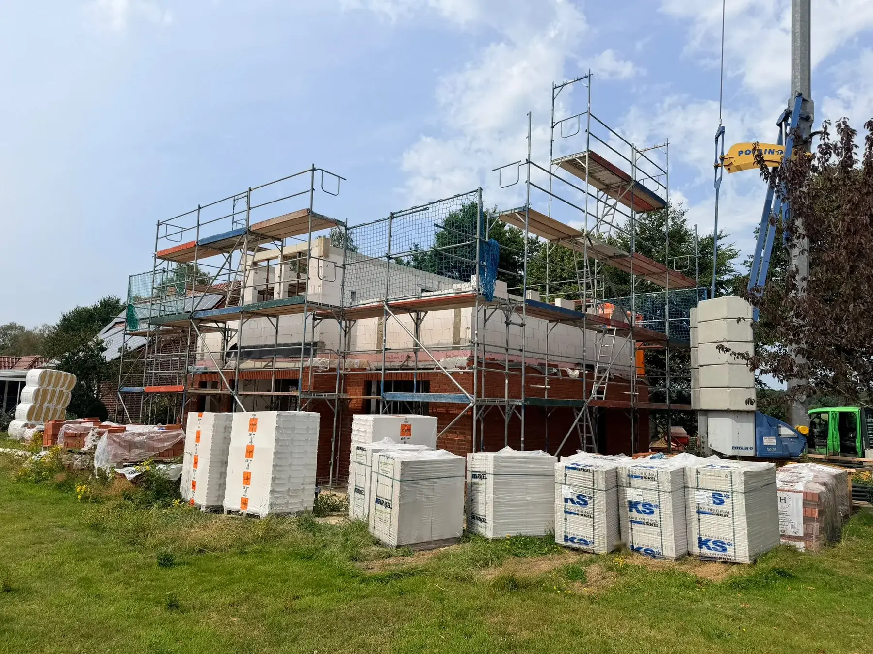 Hausneubau mit umlaufendem Gerüst und Baumaterial auf der Baustelle