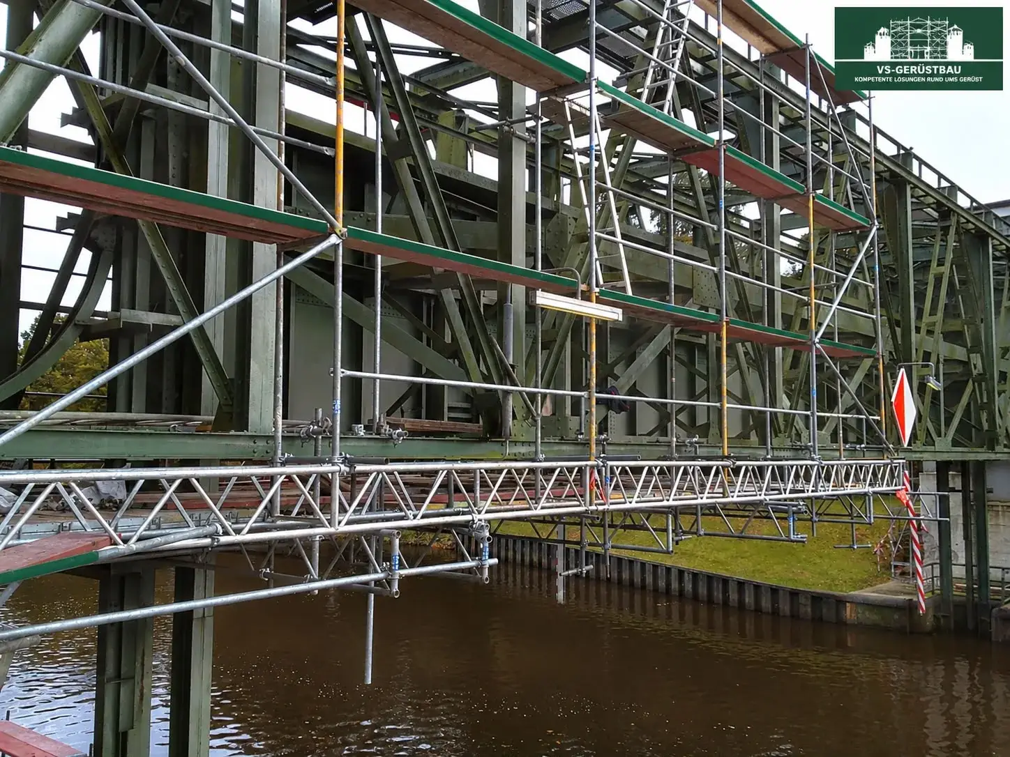 Hängegerüst mit Arbeitsplattformen an einer Stahlbrücke über einem Wasserlauf