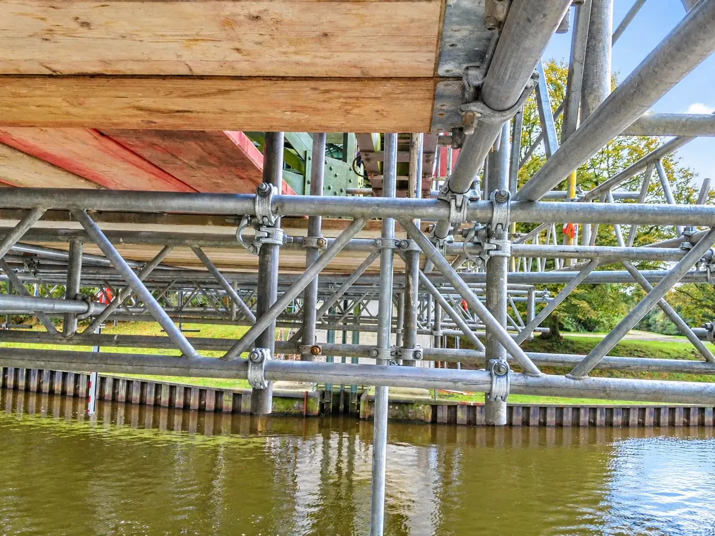 Detailansicht der Gerüstkonstruktion und Arbeitsbeläge unter einer Brücke über Wasser