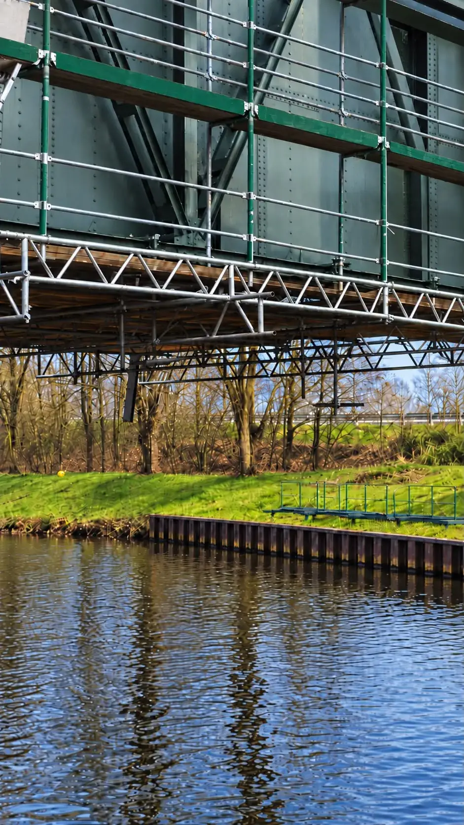 Schmale Seitenansicht eines unter einer Brücke hängenden Gerüsts über Wasser